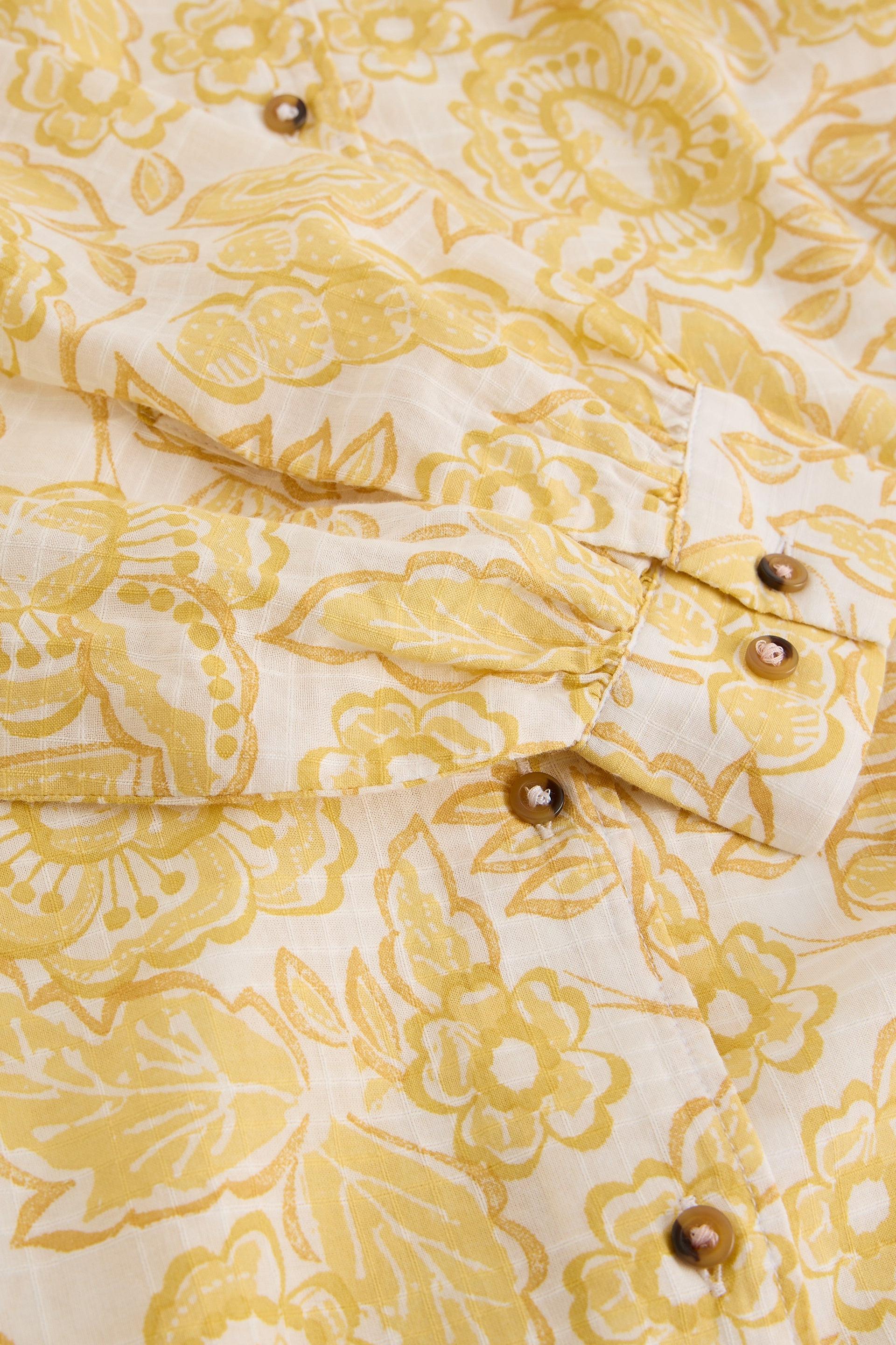 Close-up of a yellow floral organic cotton shirt with buttons.