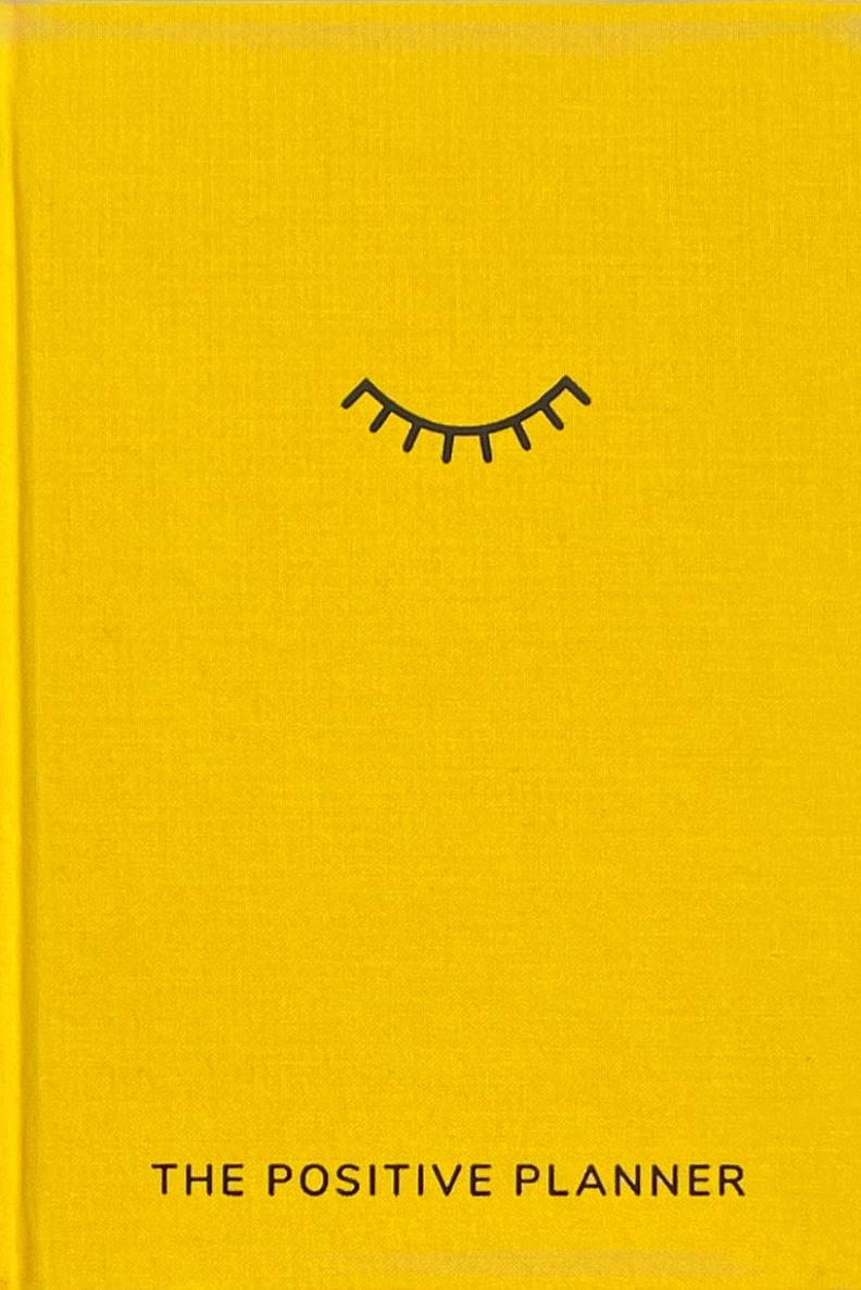 A yellow journal with a closed eye icon titled The Positive Planner, used for mindfulness and self-care.