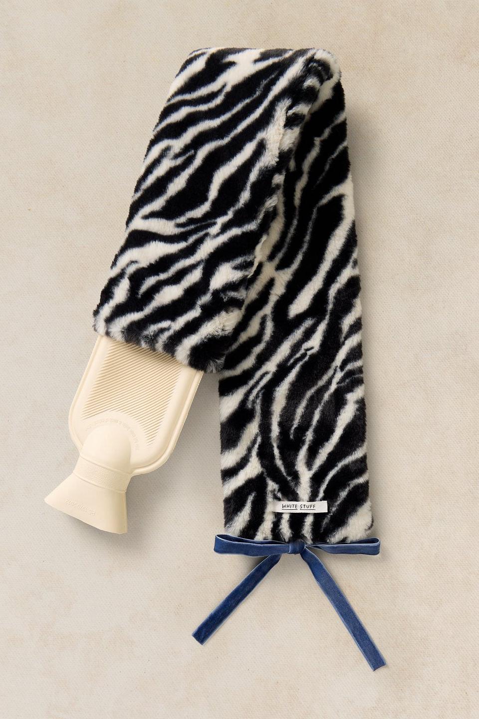 A cosy, long White Stuff hot water bottle with a fluffy black and white zebra print cover and a blue velvet ribbon tie.