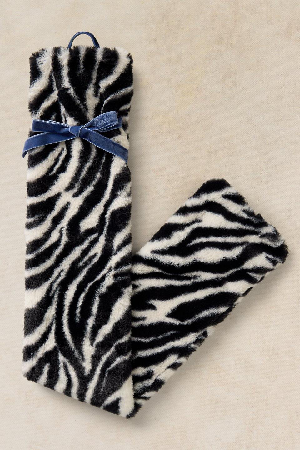 A cosy zebra print hot water bottle with a blue velvet ribbon bow, perfect as a gift for her.